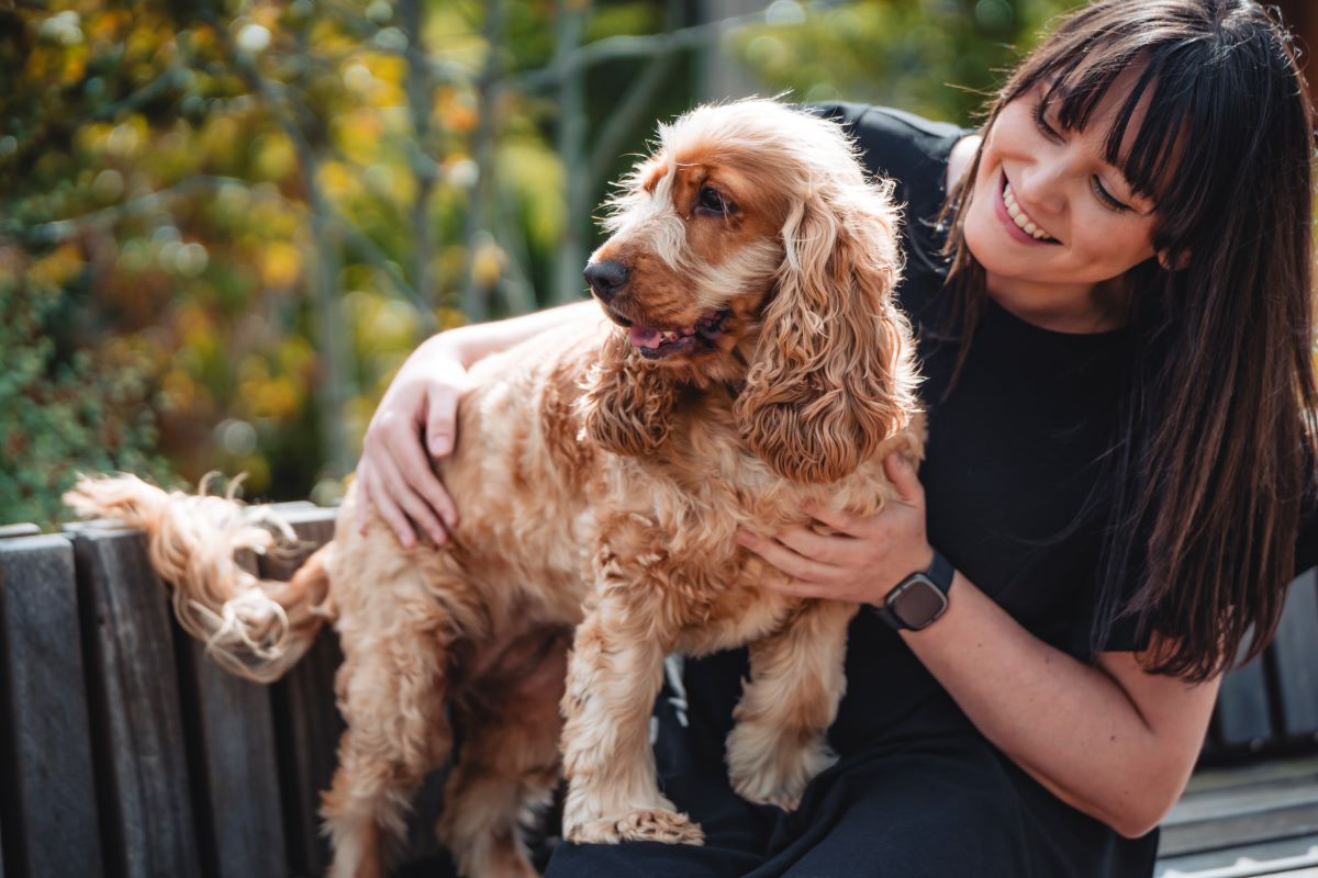 Femme souriante qui tient un chien brun dehors.