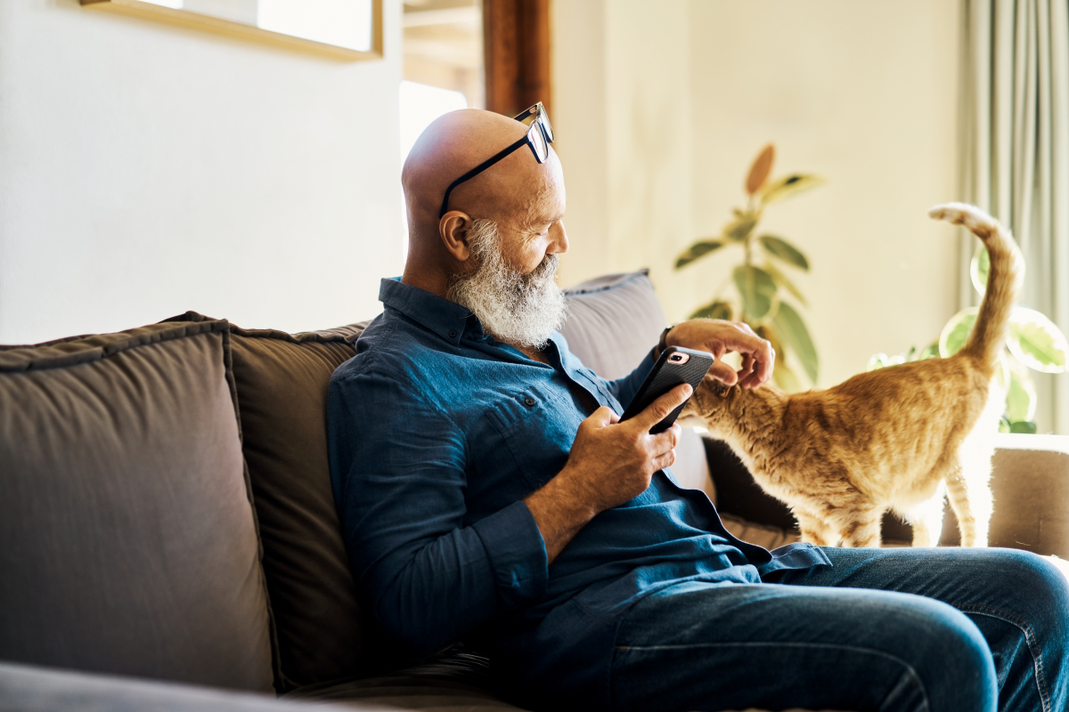 Un homme caresse un chat en tenant un téléphone sur un canapé.